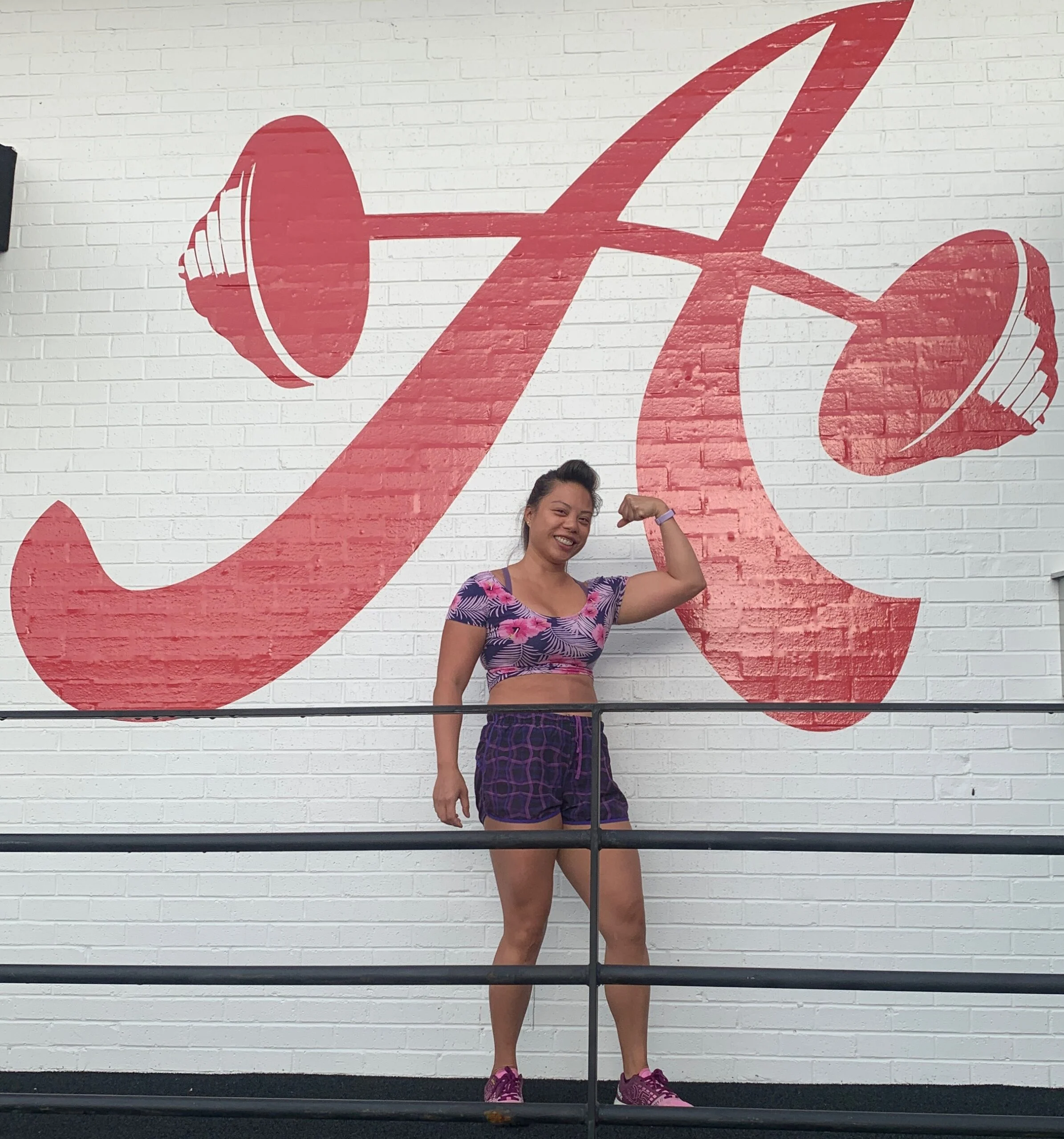 Client highlight flexing in front of the A-Barbell logo