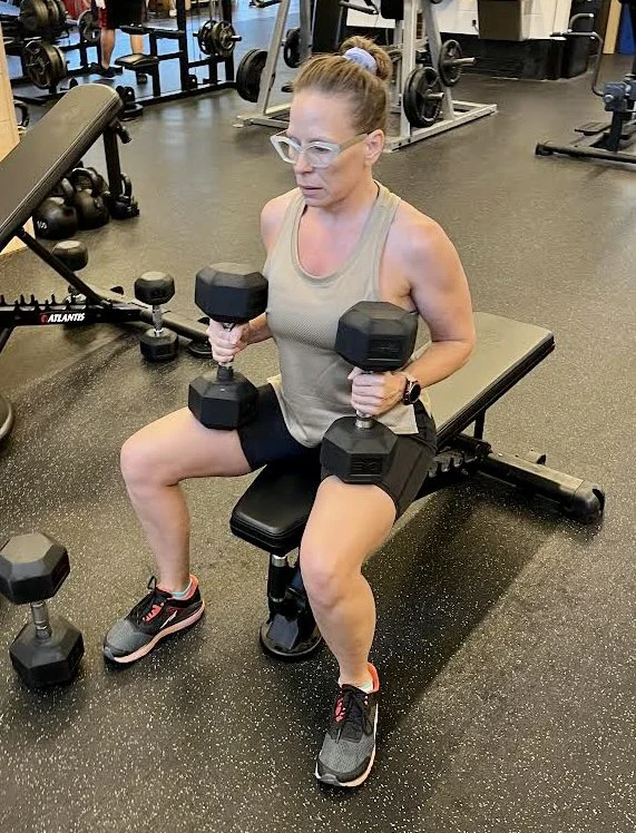 client highlight holding dumbbells and sitting on a bench