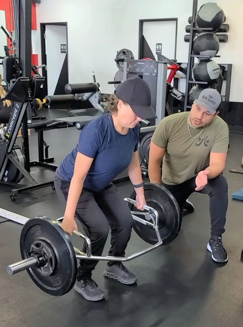 Client Highlight does a trap bar deadlift as her trainer coaches