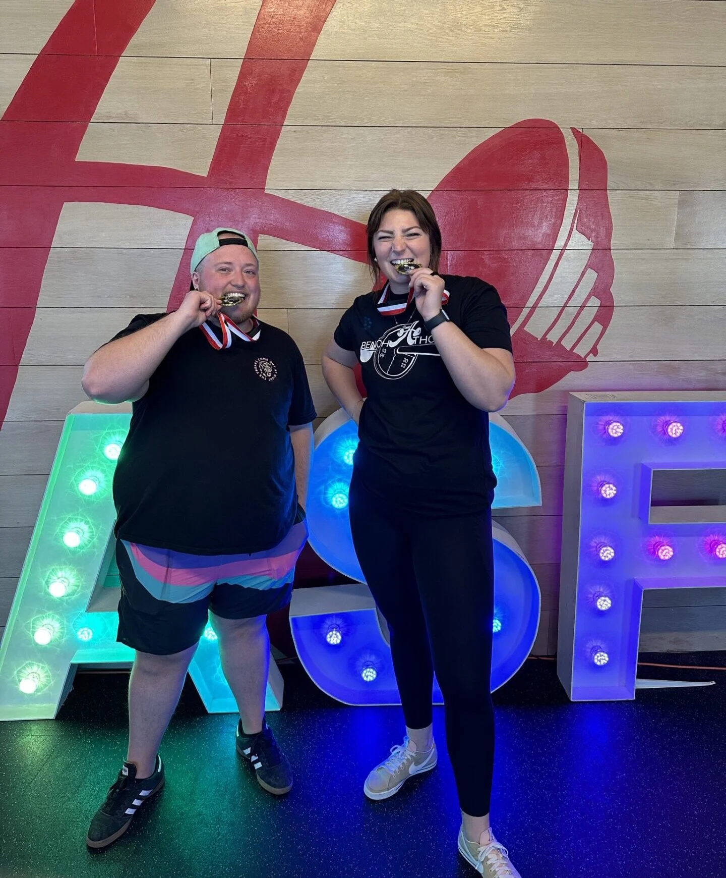 Client Highlight Jules and his trainer, Sianna biting the medals they won at Bench-A-Thon