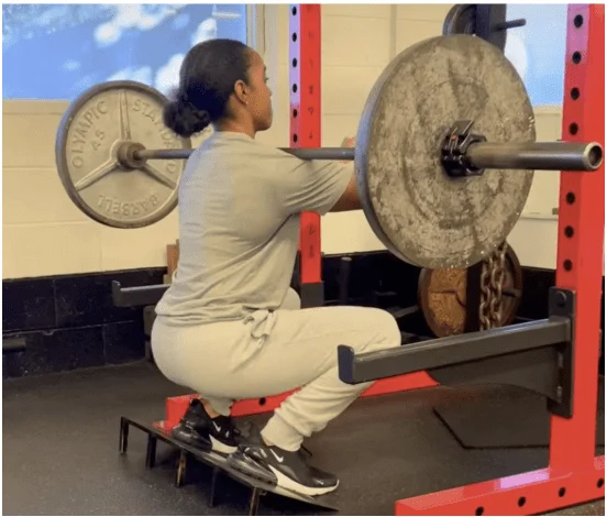 Trainer Sierra Nevels performs a barbell front squat on a slant board to full depth